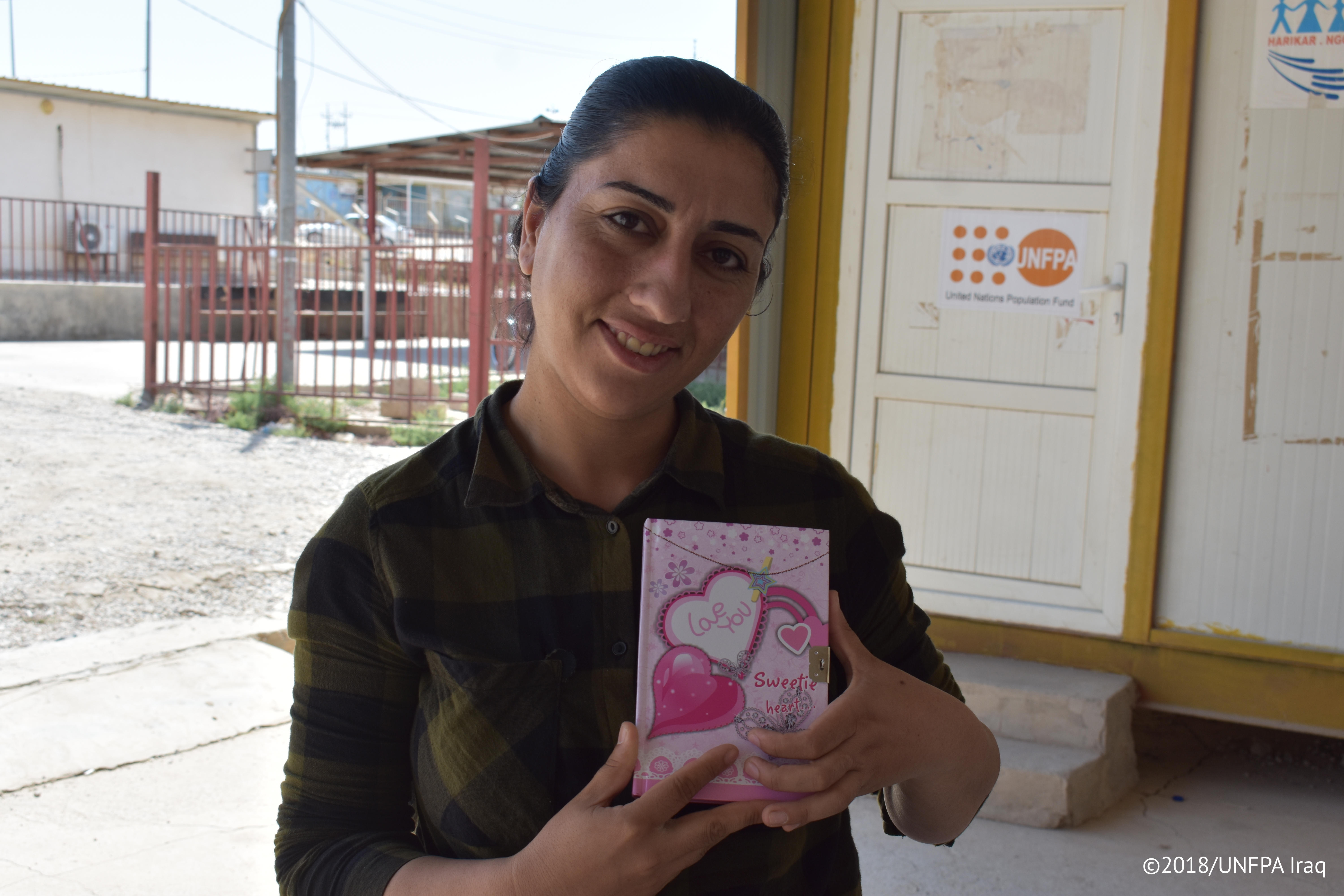 Sana’ holding her notebook where she writes down her most cherished memories since she arrived to Iraq.  © UNFPA Iraq/Salwa Moussa